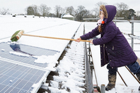Girl clears snow from a solar panel using a broom