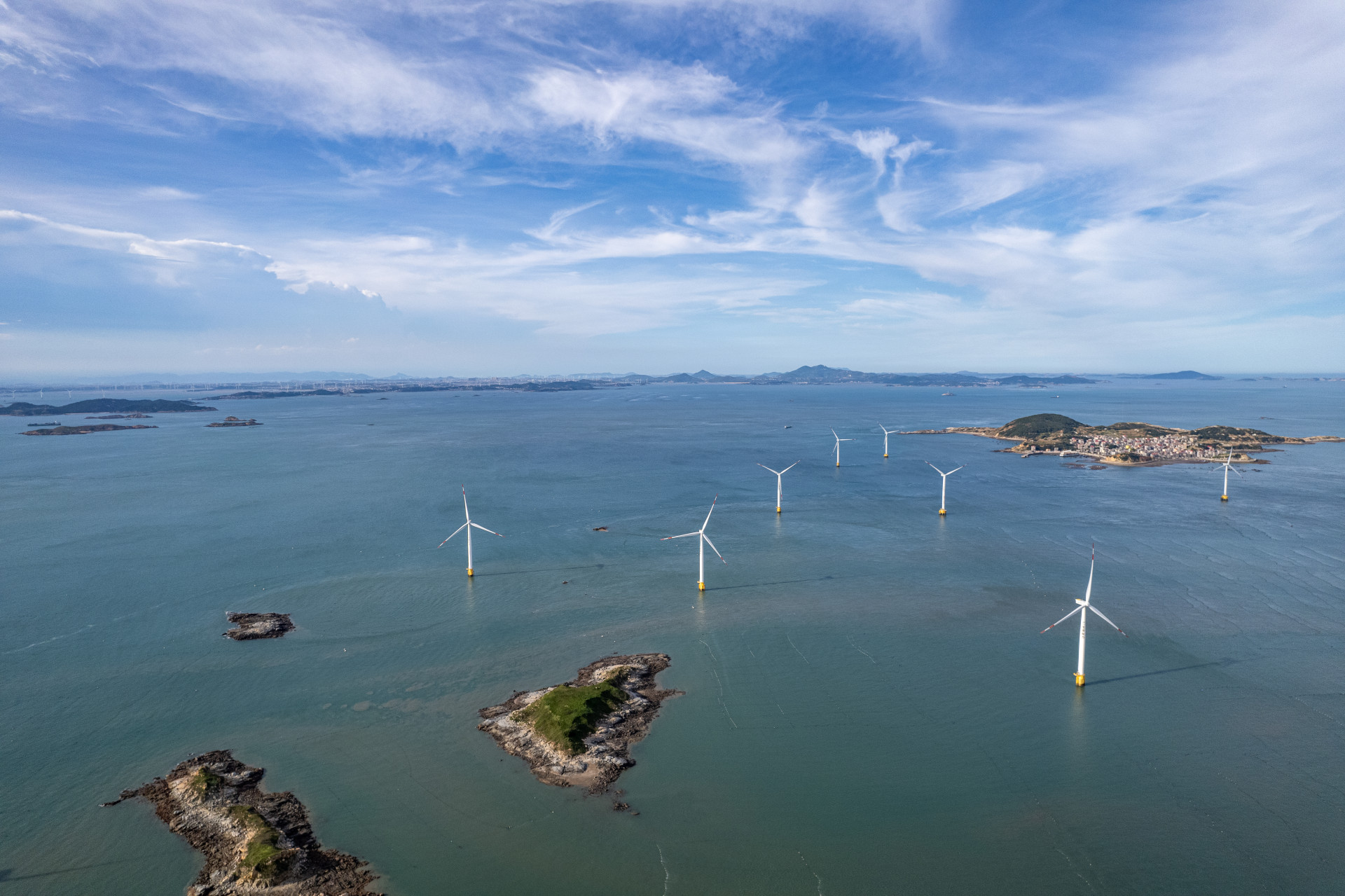 A group of wind turbines at sea on a sunny day.