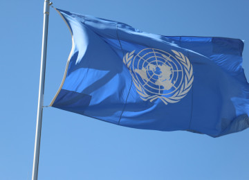 The UN flag flies in a blue sky.