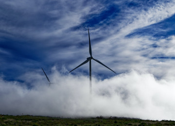 A lone windmill turns against a backdrop of blue skies and thick clouds.