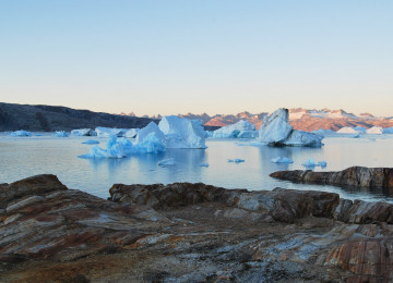 Landscape image of coastal rock with small floating glaciers at sunset in the background