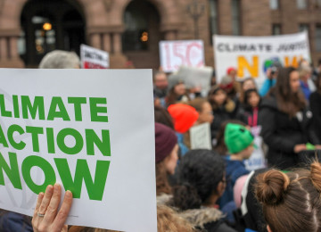 A group of people gather together, holding signs that demand climate action.