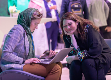 Two participants at MENA Climate Week 2023 consult information on a laptop.