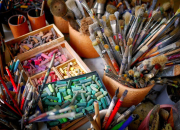 Colourful paint brushes and pastel chalk on a desk.