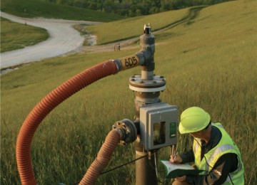 Man in high-vis kneels beside landfill gas pipe in a field