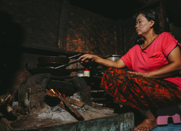 woman cooking with old woodfire cookstove which this project will replace