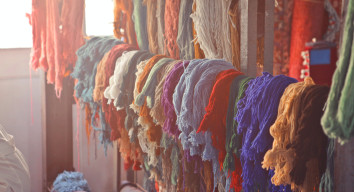 A rack of different coloured fabrics hang on a rack in the sun.