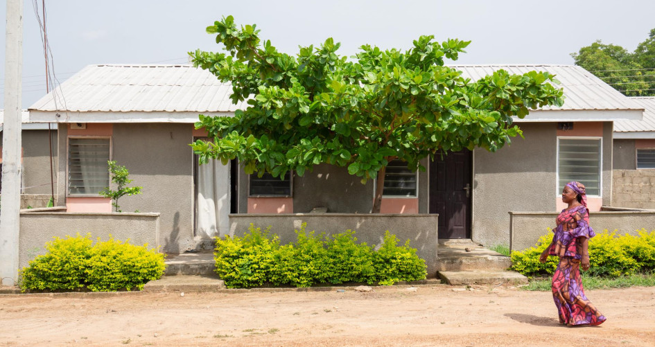 Image of a woman walking by a house built by Reall Housing in Africa
