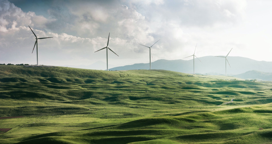 A row of windmills stand atop a bank of grassy, green hills.