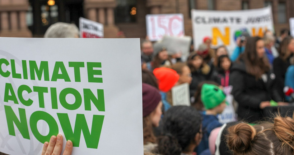 A group of people gather together, holding signs that demand climate action.