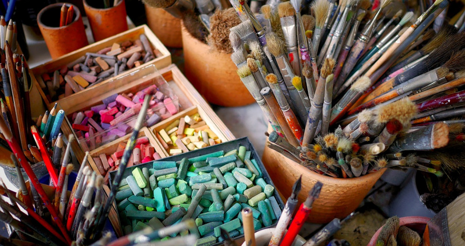 Colourful paint brushes and pastel chalk on a desk.