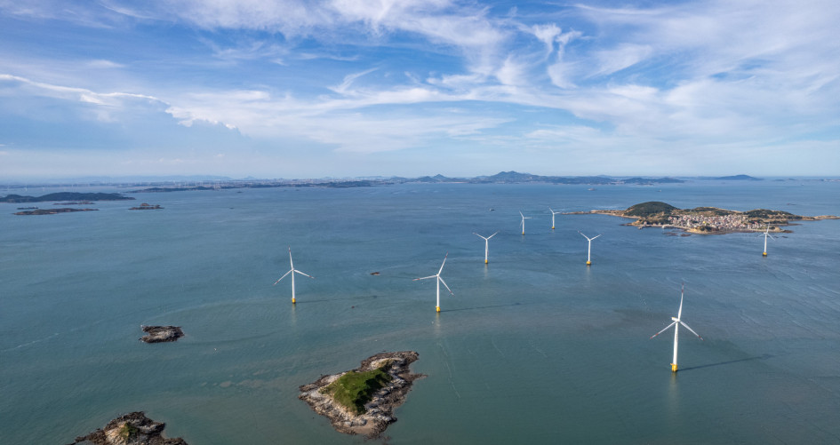 A group of wind turbines at sea on a sunny day.