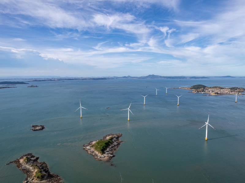 A group of wind turbines at sea on a sunny day.