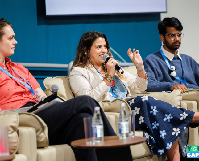 Three panelists, one of them speaking into microphone, the others listening