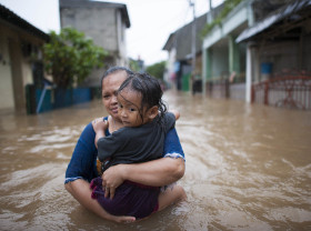 A woman and her child make their way precariously through a flooded street in Indonesia. 