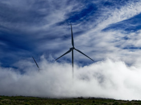 A lone windmill turns against a backdrop of blue skies and thick clouds.