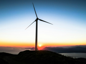 A windmill stands on a hill as the sun sets behind it.