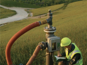 Man in high-vis kneels beside landfill gas pipe in a field