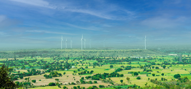 Wind turbines towering over green fields under a clear blue sky in Rajapur, India